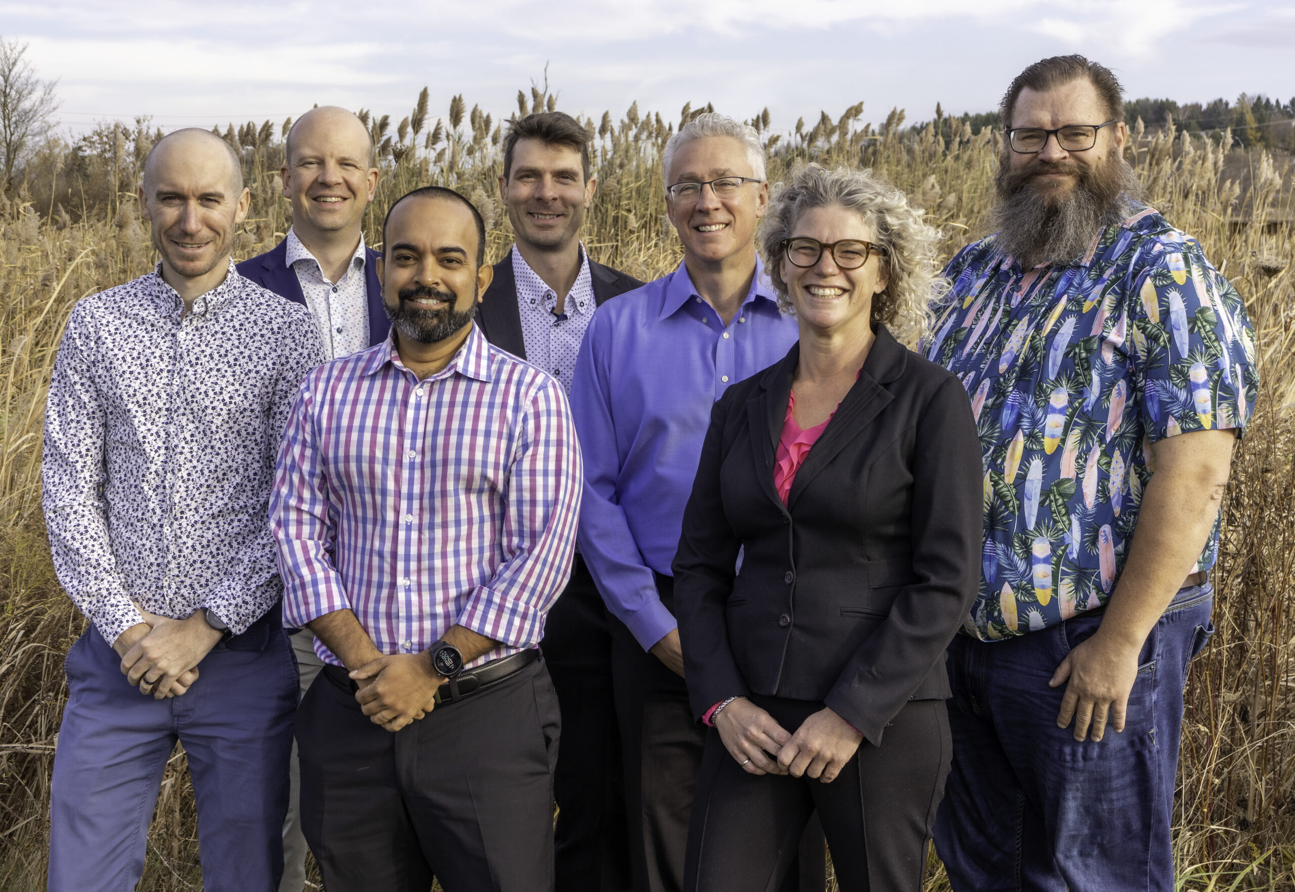 A group of 6 men and one women standing together in front of a field