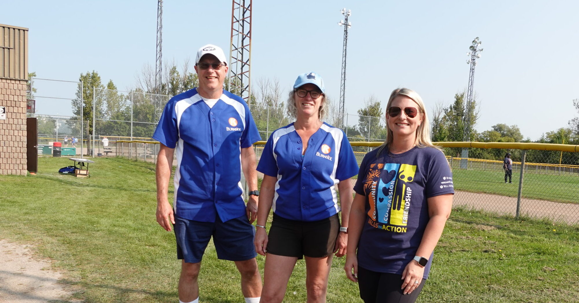 A man and two women standing together in front of a baseball diamond