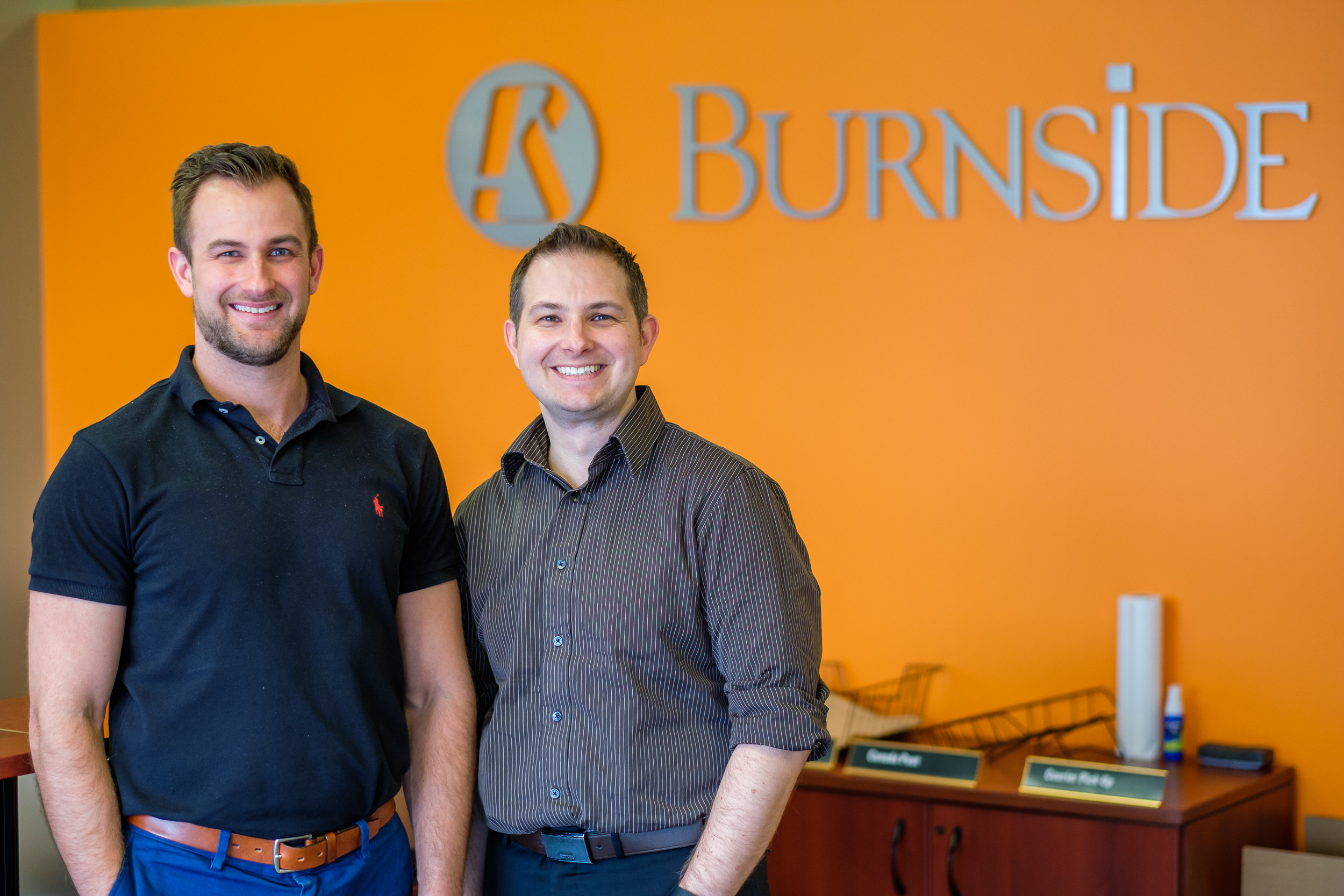 Two men standing in front of a sign smiling