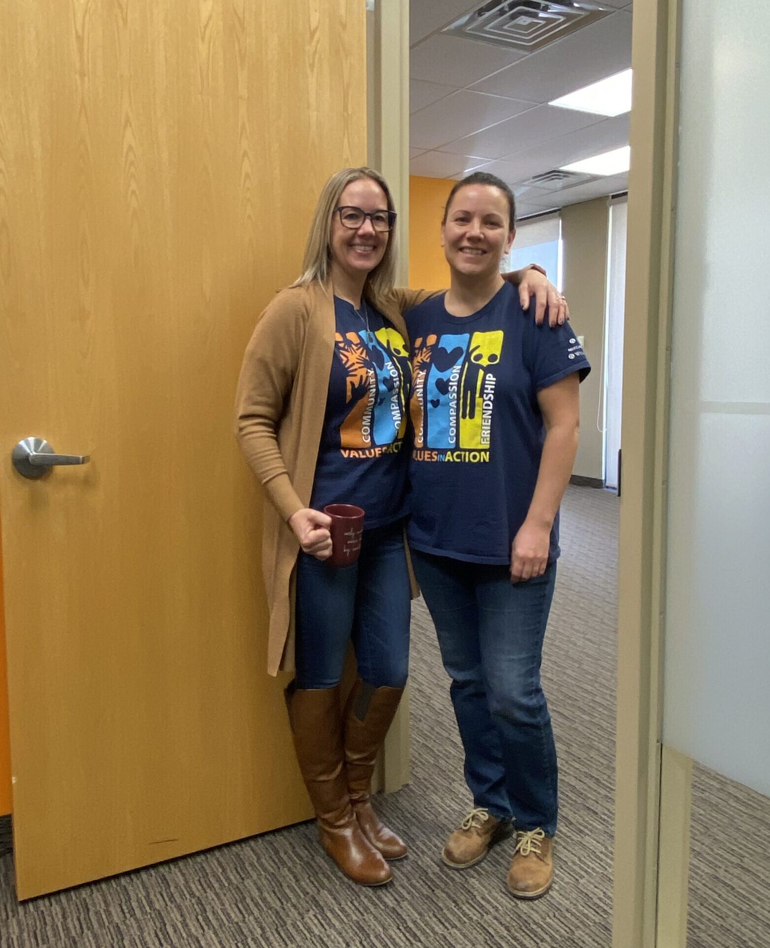 Two women standing in door of an office with arm around each other smiling.